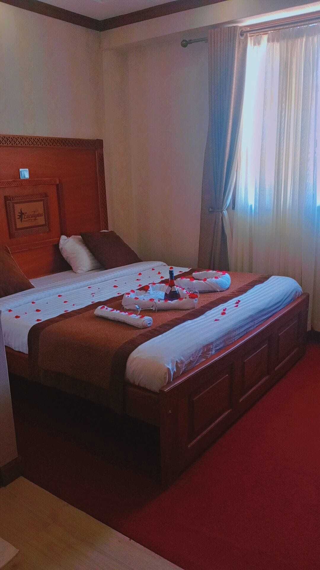 Habitación de hotel con una cama grande, cabecera de madera, un pequeño marco de fotos y una ventana con cortinas.