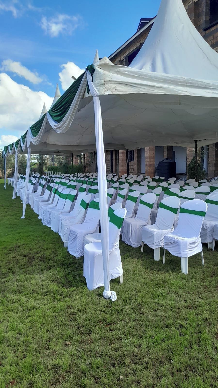 A tented outdoor event space with rows of white chairs and green sashes.