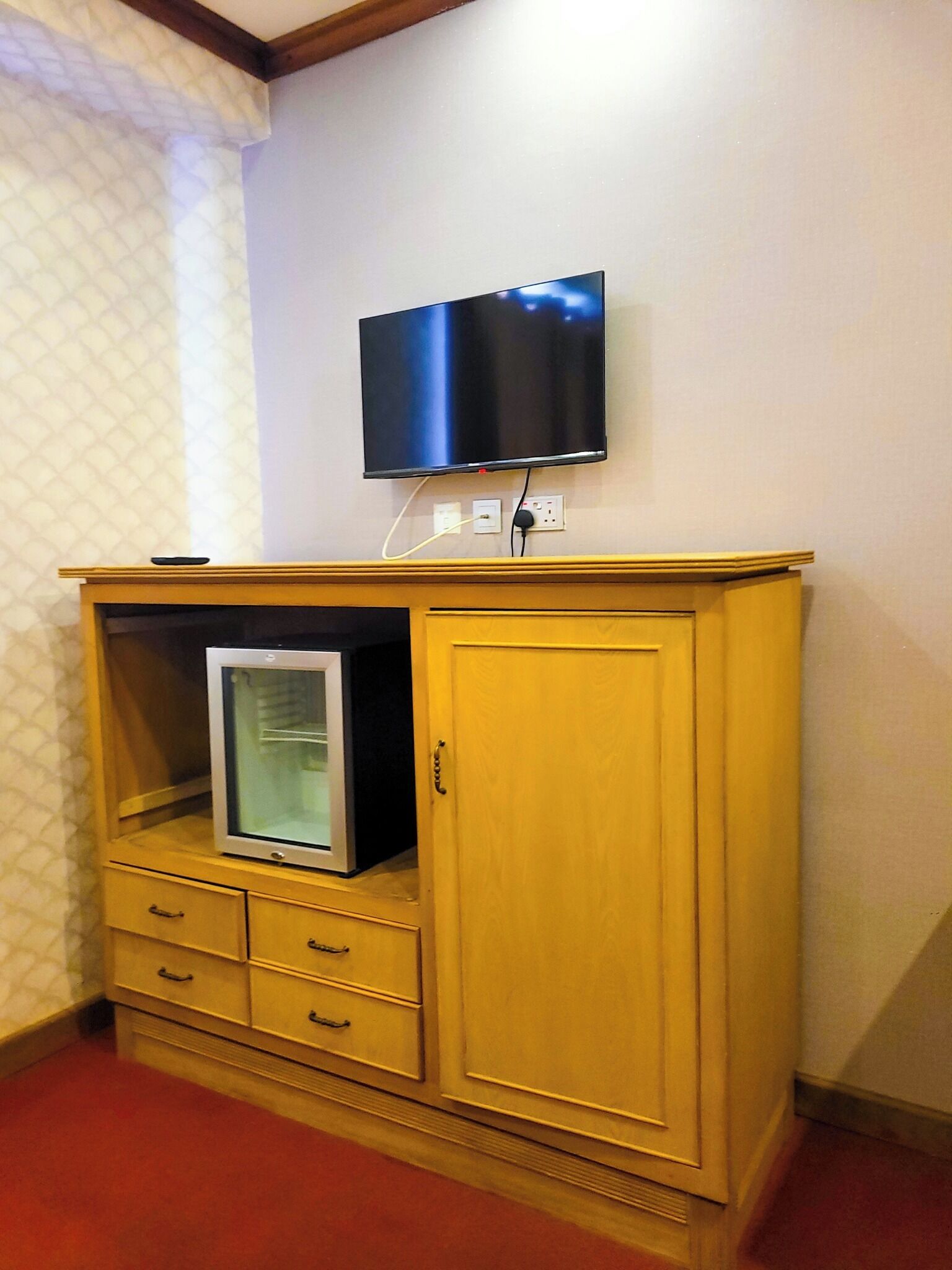 A wooden cabinet with a television mounted above it, a small refrigerator inside, and a power outlet on the wall.