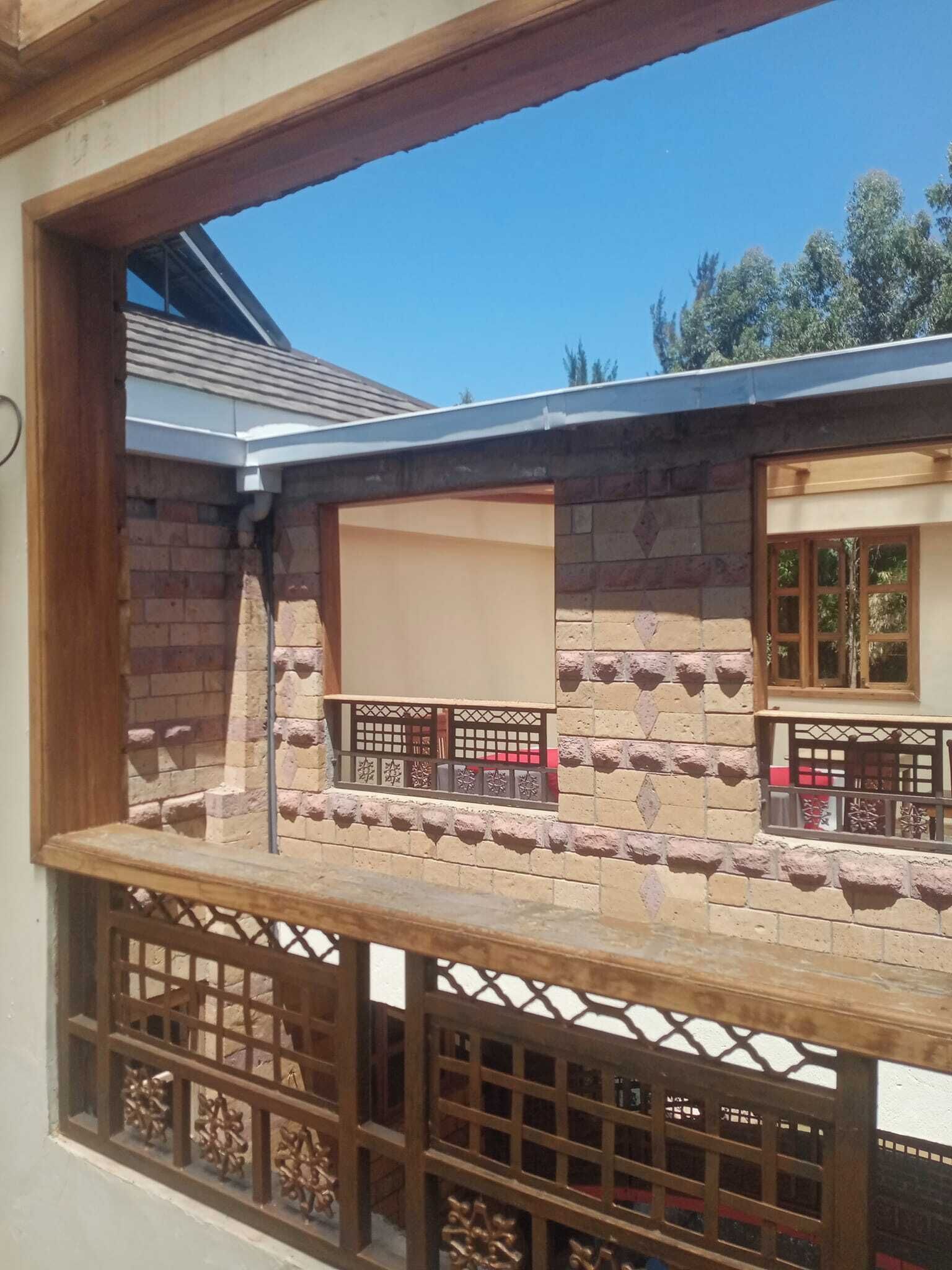 A balcony with a stone wall, wooden railing, and a window with a view of a tree.