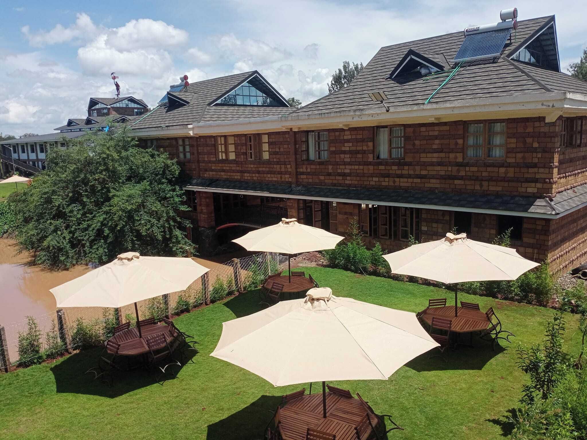 A brick building with a sloped roof, outdoor seating with umbrellas, and a small pond.