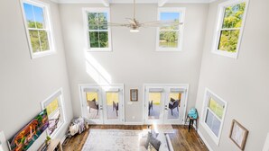Une pièce spacieuse avec un plafond haut, de grandes fenêtres et un ventilateur de plafond.