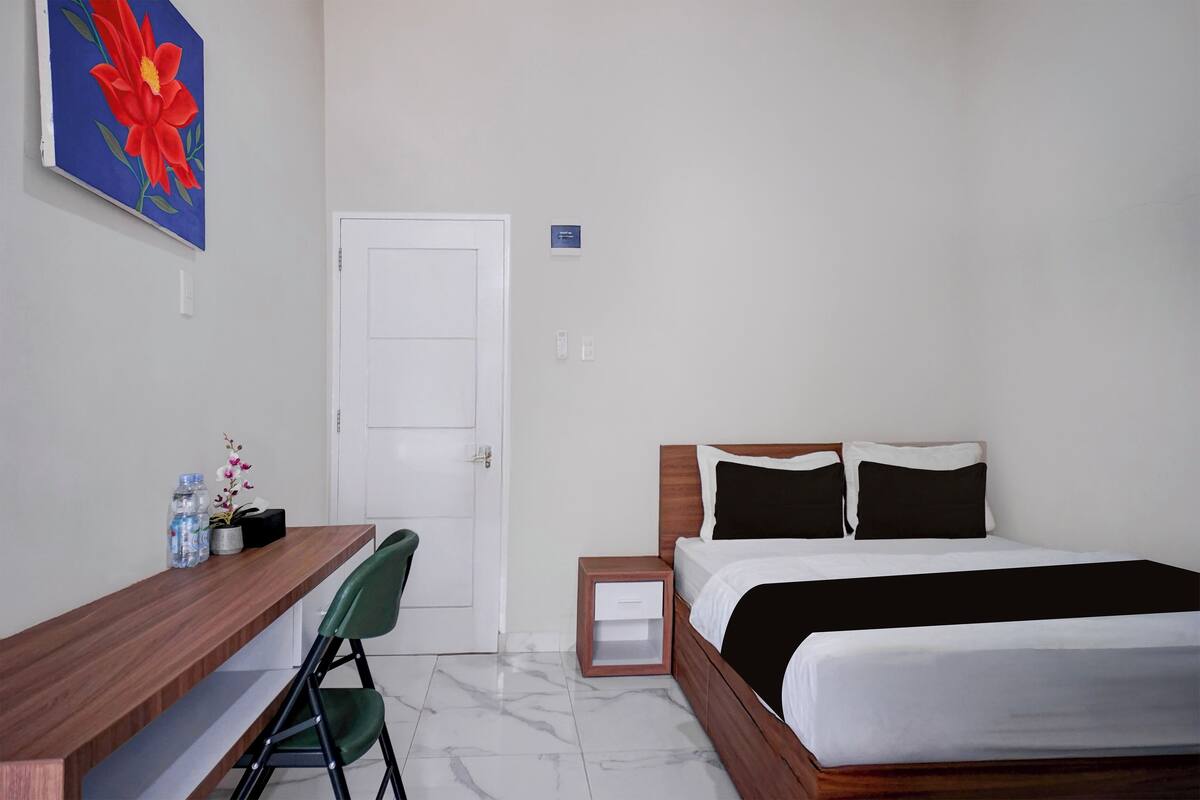 Een hotelkamer met een houten bureau, een bed met zwart-wit beddengoed, een klein nachtkastje en een deur.