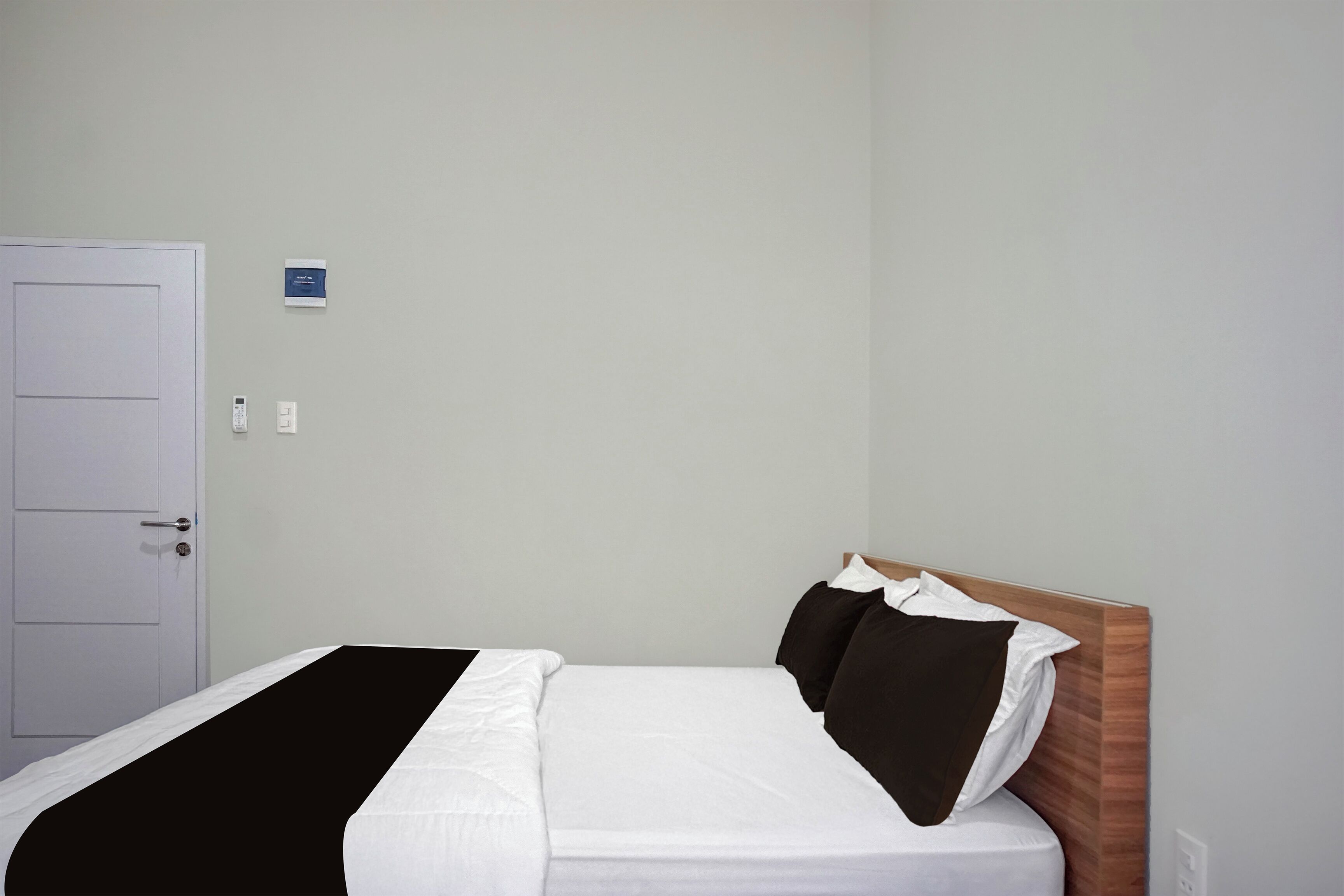 A hotel room with a bed, a door, and a wall-mounted control panel.