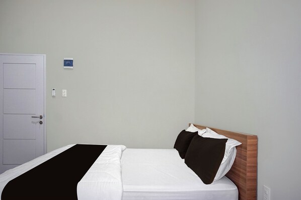 A hotel room with a bed, a door, and a wall-mounted control panel.