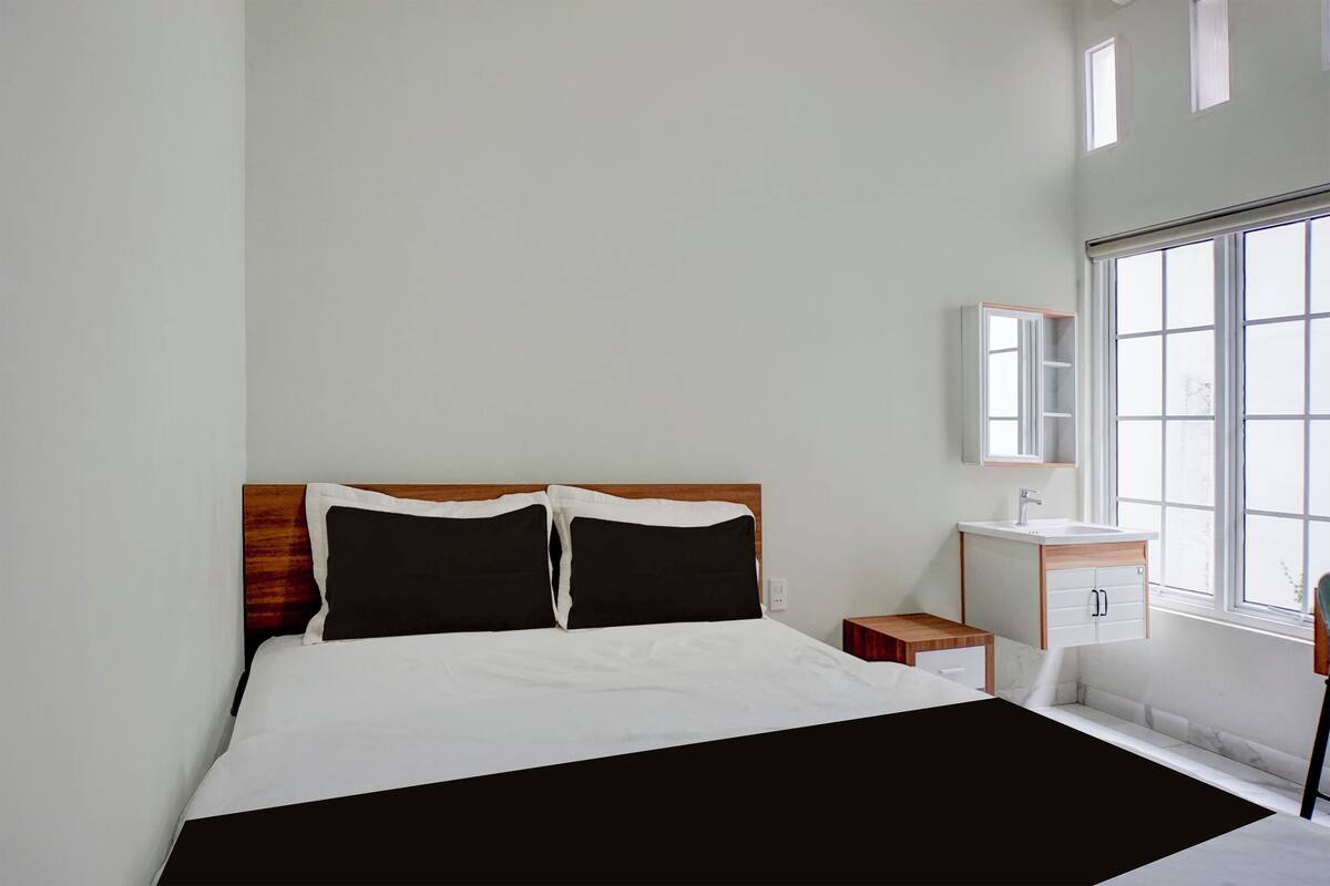 Een moderne slaapkamer met een groot bed, een houten hoofdbord, een klein nachtkastje, een inbouwspoelbak en een raam met uitzicht.