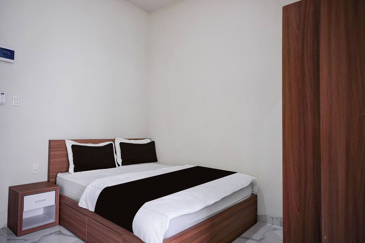 Een keurig opgemaakt slaapkamer met een houten bedframe, een nachtkastje met een lade, en een witte muur.