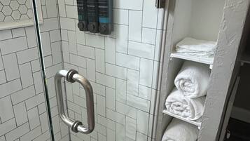 A shower area with hexagonal tiles, a glass door, a metal grab bar, and a shelf with towels.