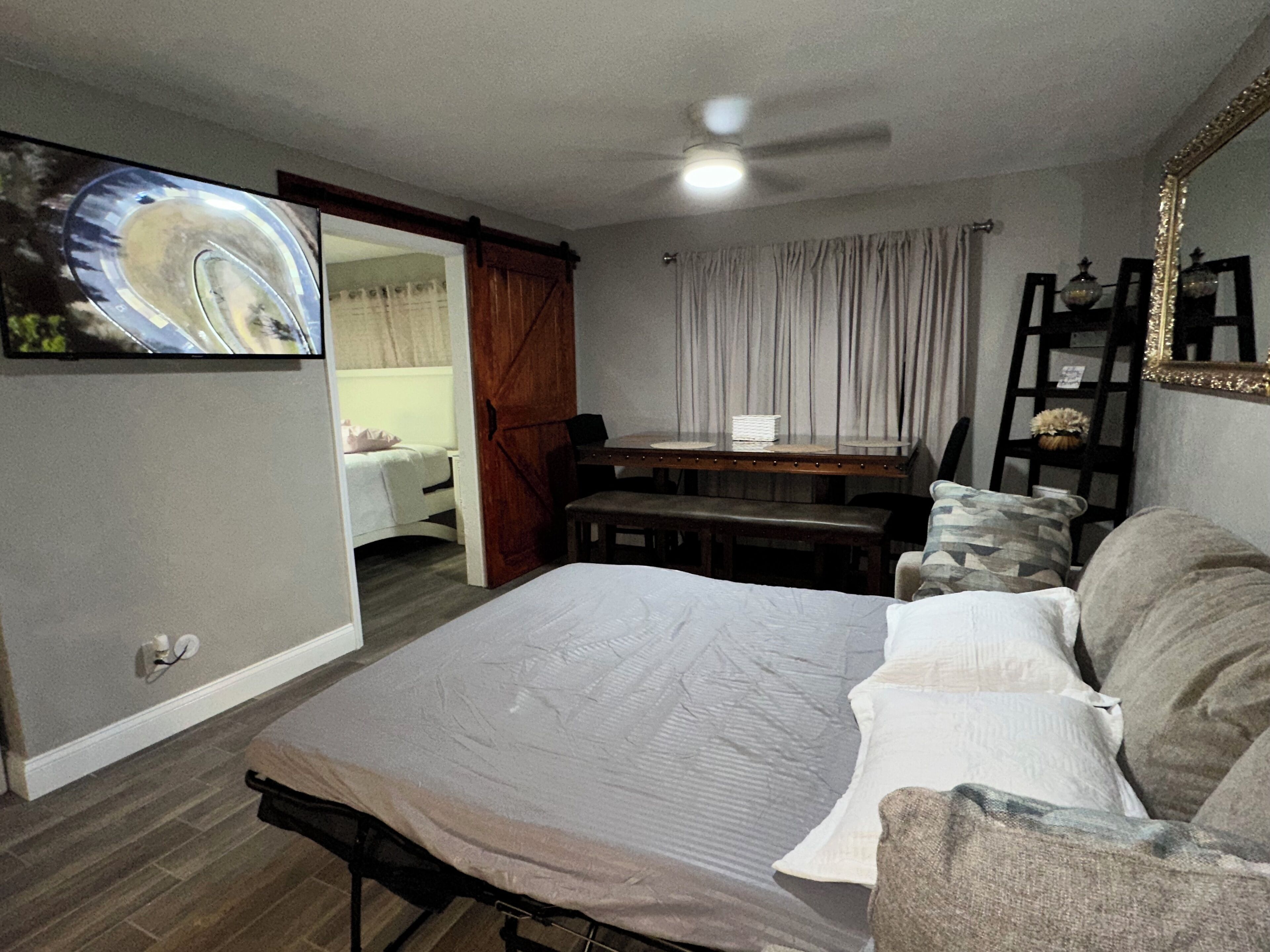 A bedroom with a bed, a TV mounted on the wall, a dining table with chairs, and a mirror on the wall.