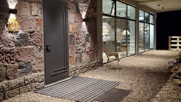 A stone-walled room with a door, a chair, and a window.