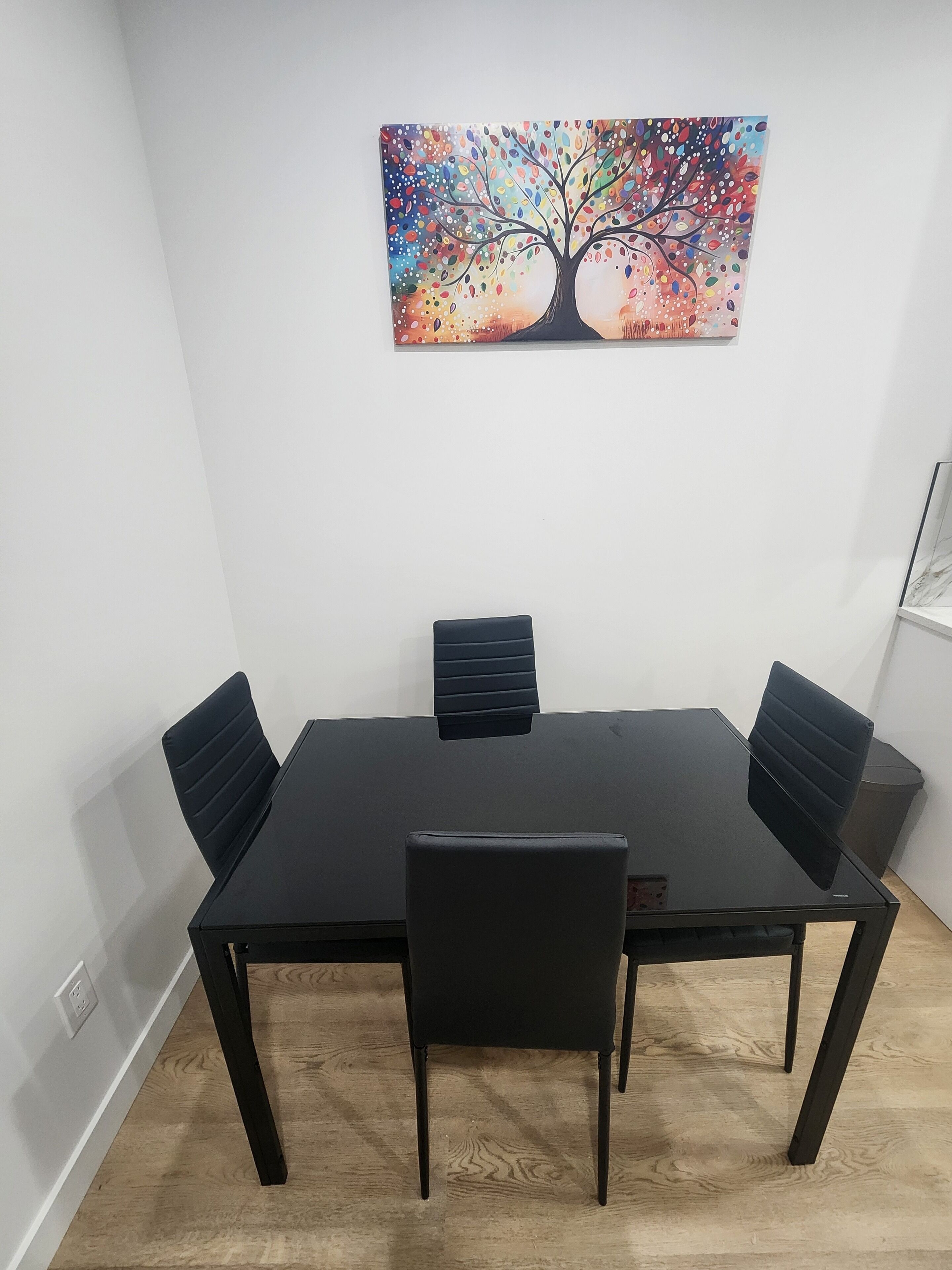 A conference room with a black table, four black chairs, and a colorful tree painting on the wall.