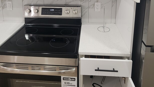 A modern kitchen with a stainless steel microwave, a black stove, and a coffee maker on a shelf.