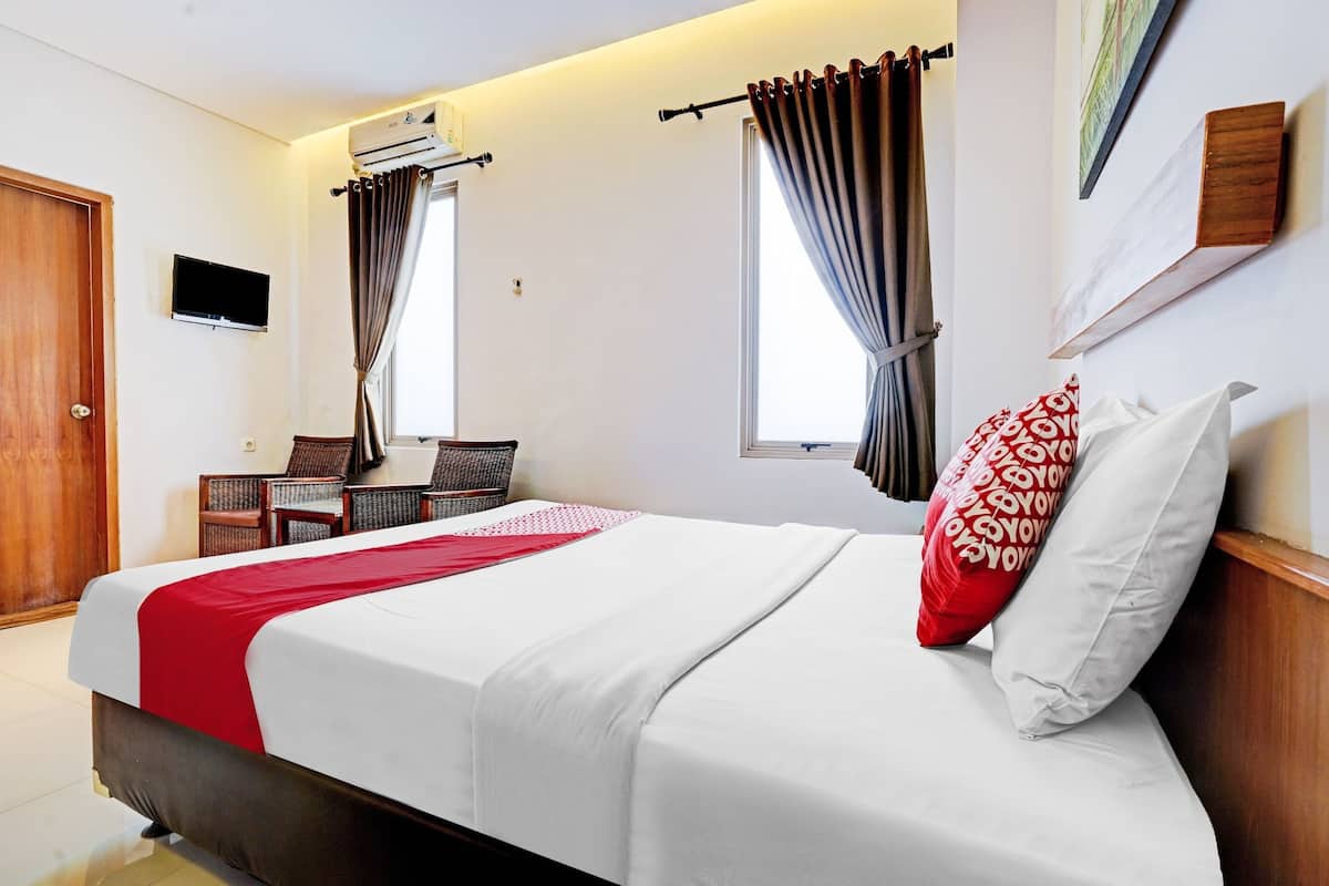 Una habitación de hotel con cama, televisión, escritorio y dos ventanas con cortinas.