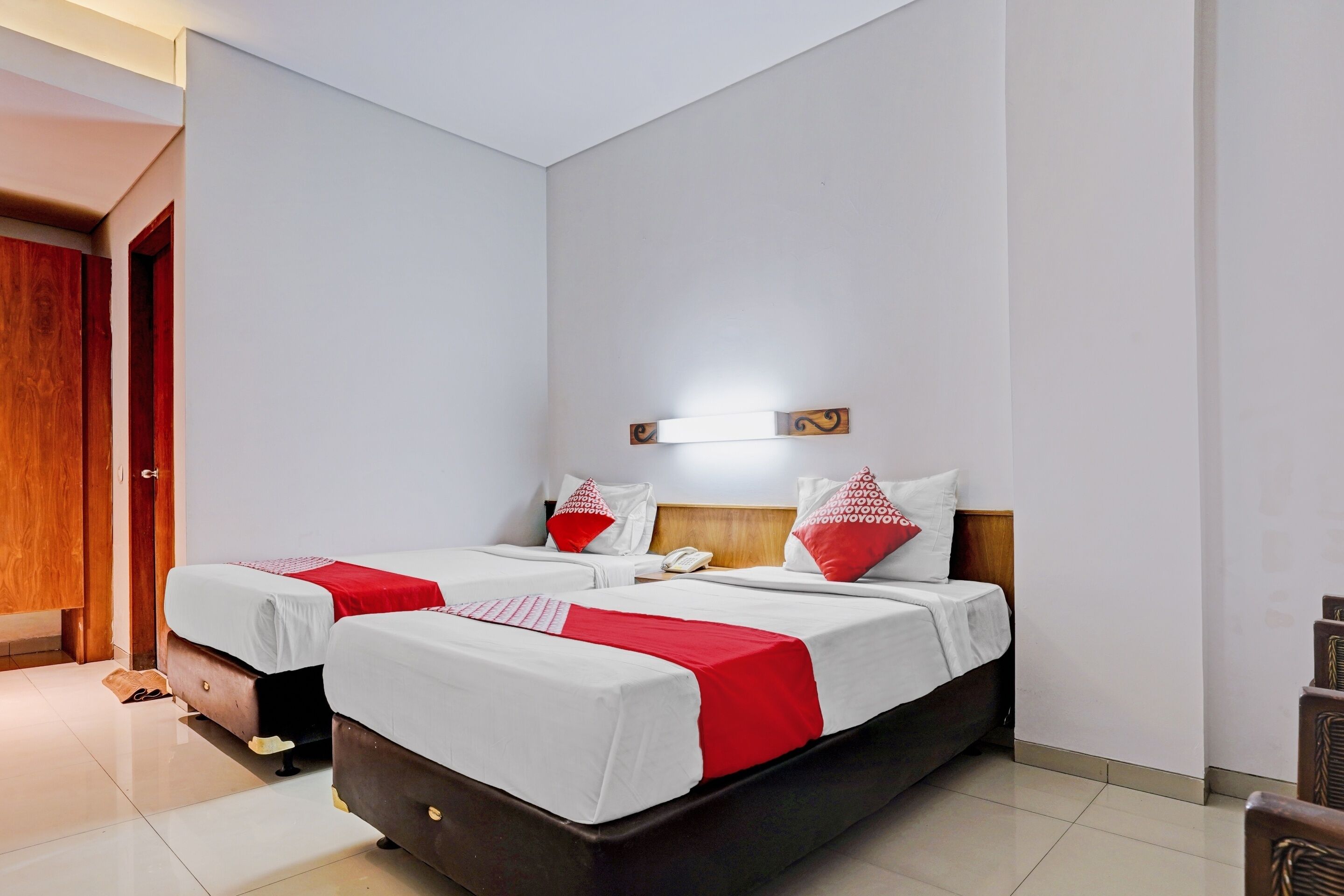 Quarto de hotel com duas camas, um guarda-roupa de madeira, uma mesa de cabeceira e um candeeiro fixado na parede.