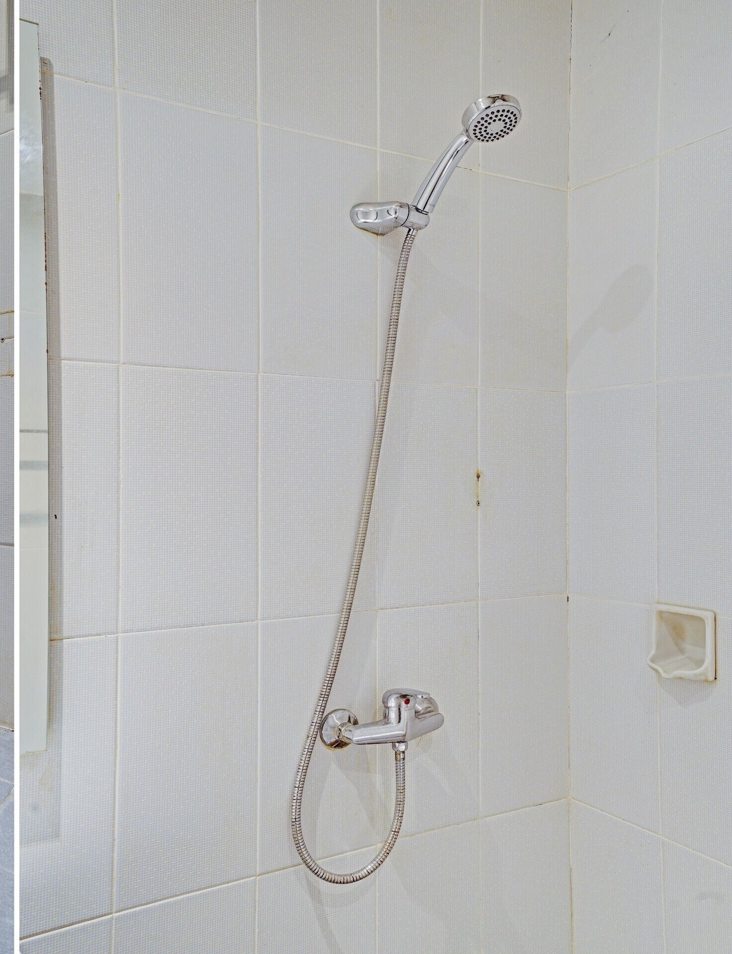 A shower with a handheld showerhead and a fixed showerhead, mounted on a tiled wall.