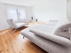 A modern living room with a sofa, a chair, a small round table, and a window with sheer curtains.