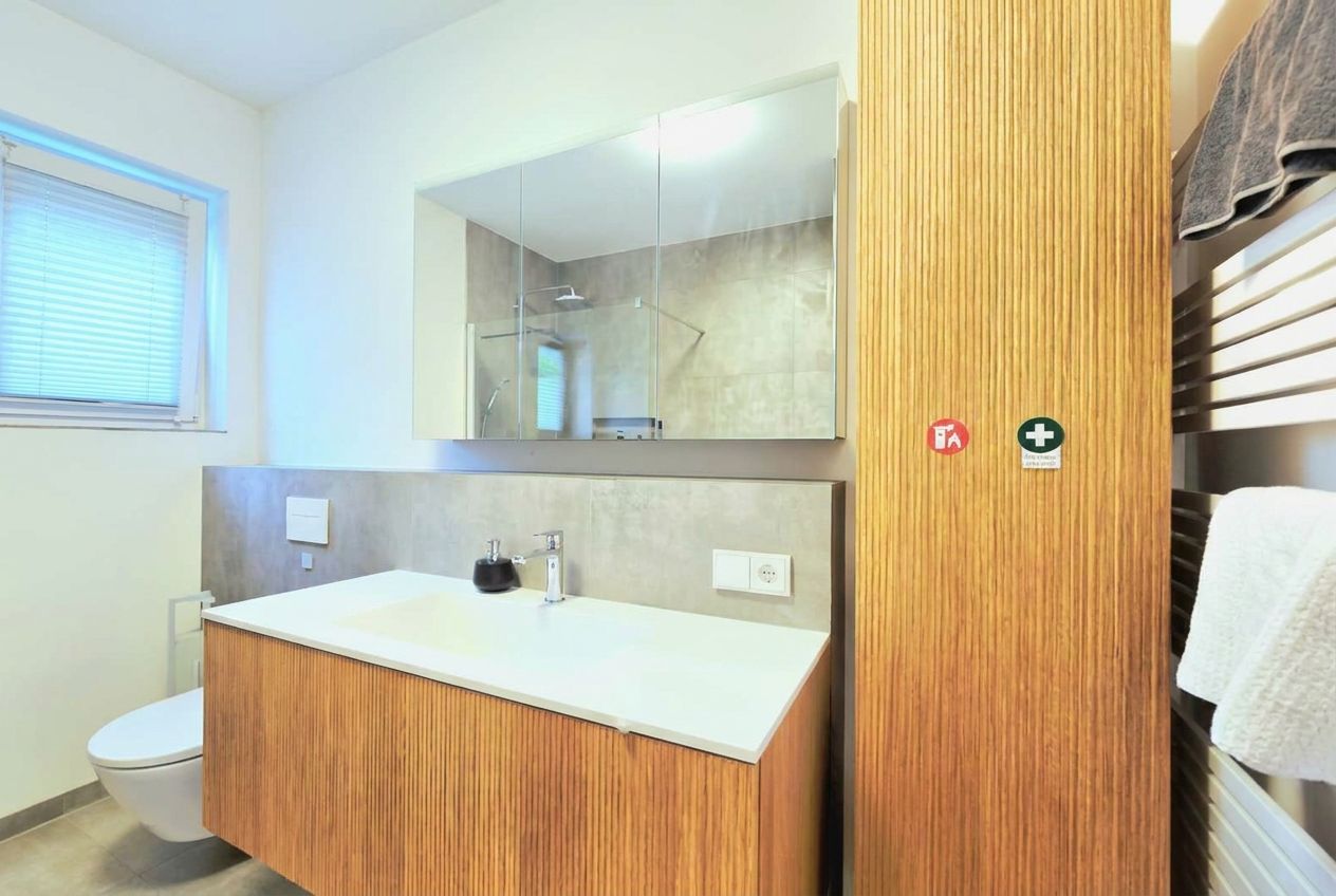 A modern bathroom with a wooden vanity, a large mirror, and a shower area.
