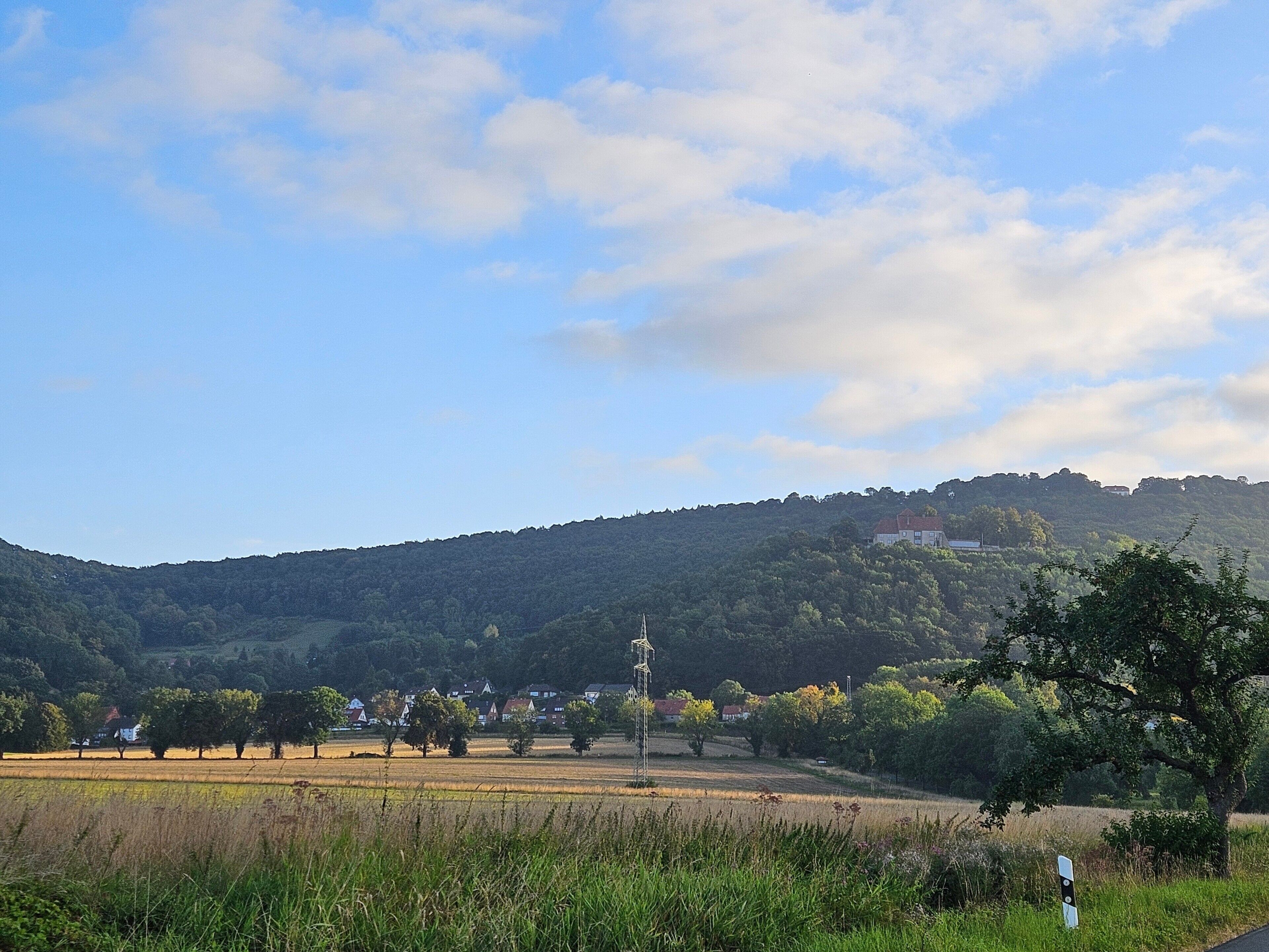 A rural landscape with a hill, trees, and a few buildings.