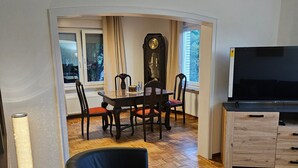 Una sala de estar con una mesa de comedor, sillas, un reloj, un televisor y un sofá.
