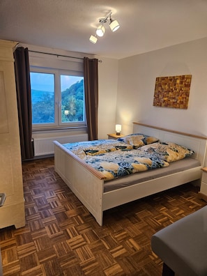 A bedroom with a bed, a window with curtains, a radiator, a wooden floor, and a wall-mounted light fixture. - Apartment 'Panoramablick' with Mountain View and Wi-Fi (Rinteln)