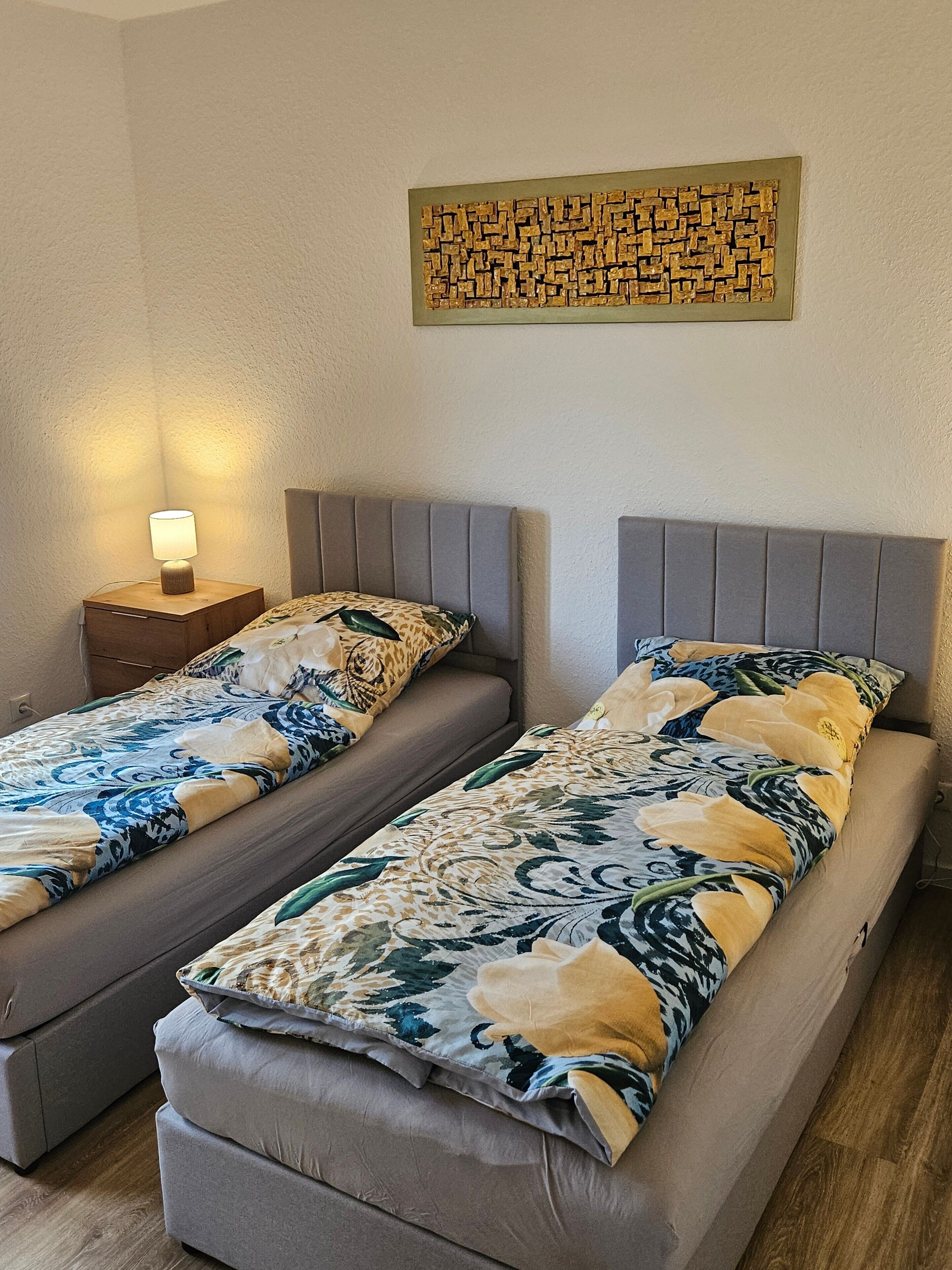 Una habitación con dos camas, una mesita de noche con lámpara y un adorno en la pared.
