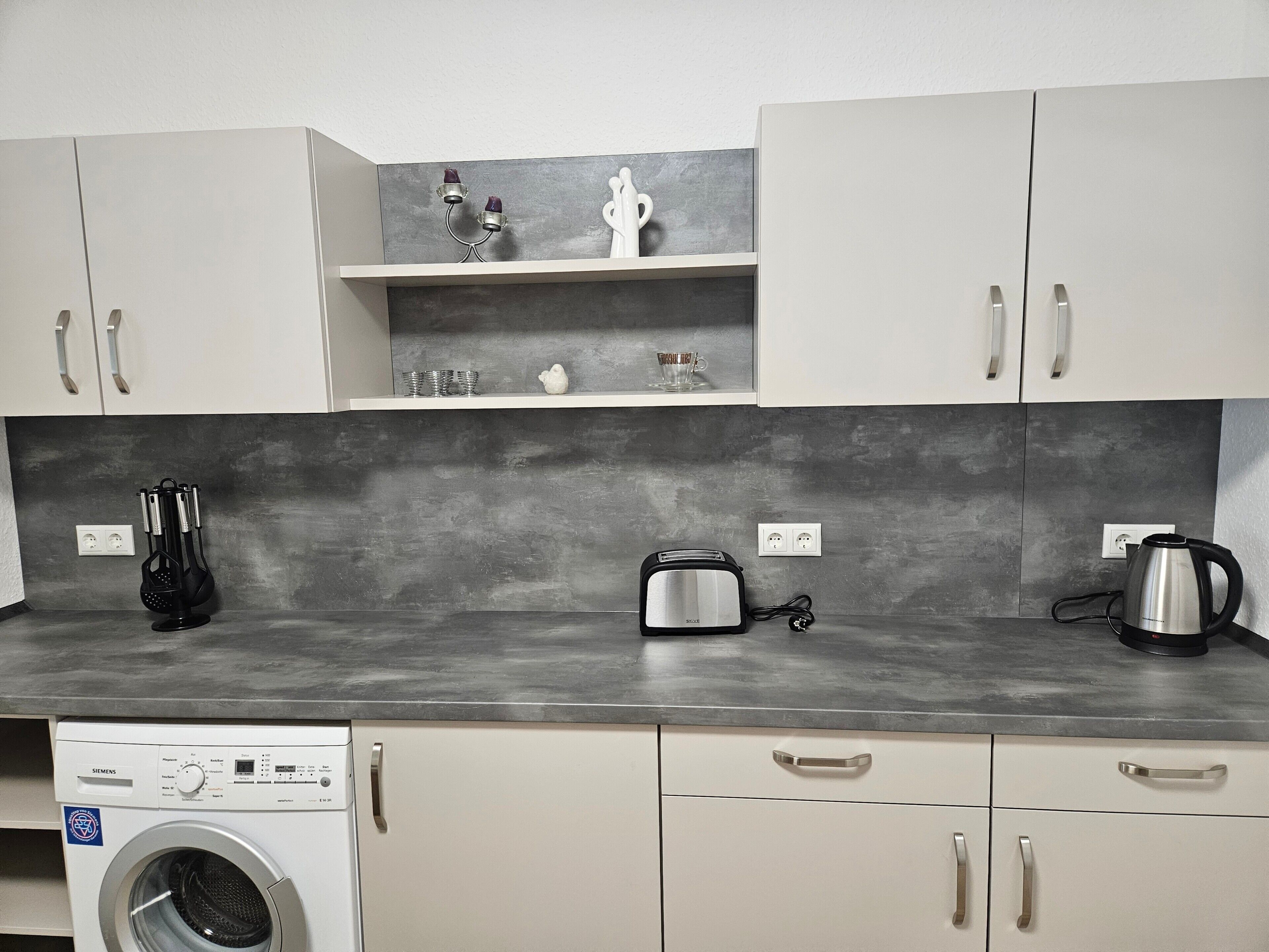 Una cucina compatta con lavatrice, tostapane e bollitore.