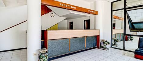 A reception area with a wooden reception desk, a clock, and a staircase leading to upper floors.