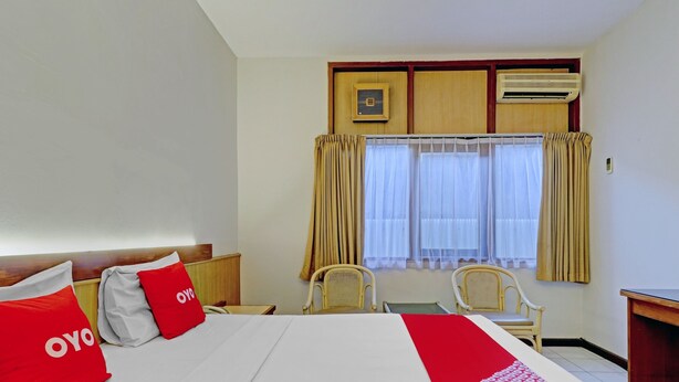 A hotel room with a bed, two chairs, a desk, and a window with curtains. - OYO 94726 Asteria Talaga Bodas (Bandung)