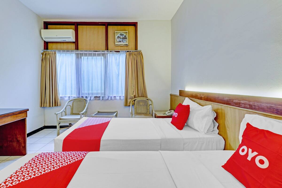 Une chambre d’hôtel avec deux lits, un bureau, une chaise et une fenêtre avec des rideaux.