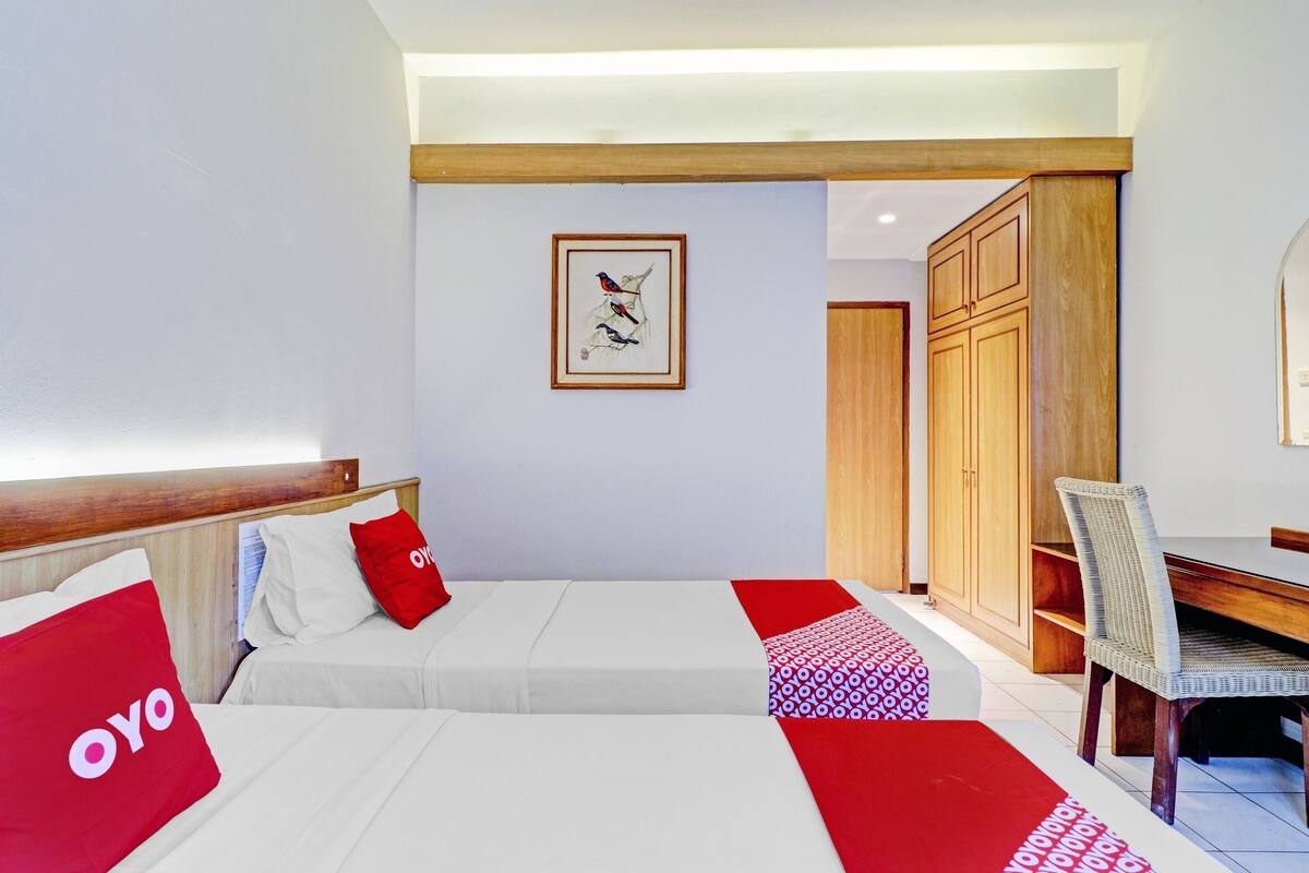 Une chambre d’hôtel avec deux lits, une armoire en bois, une table à manger et une œuvre d’art encadrée au mur.