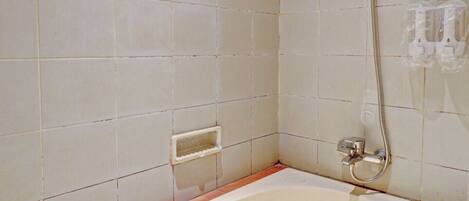 A bathroom with a bathtub, a showerhead, and a wall-mounted faucet.