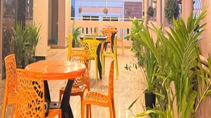 A dining area with orange chairs and tables, surrounded by potted plants. - Le Avirah (Vanur)