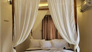 A four-poster bed with white linens and drapes, a ceiling fan, and a tiled floor. - Le Avirah (Vanur)