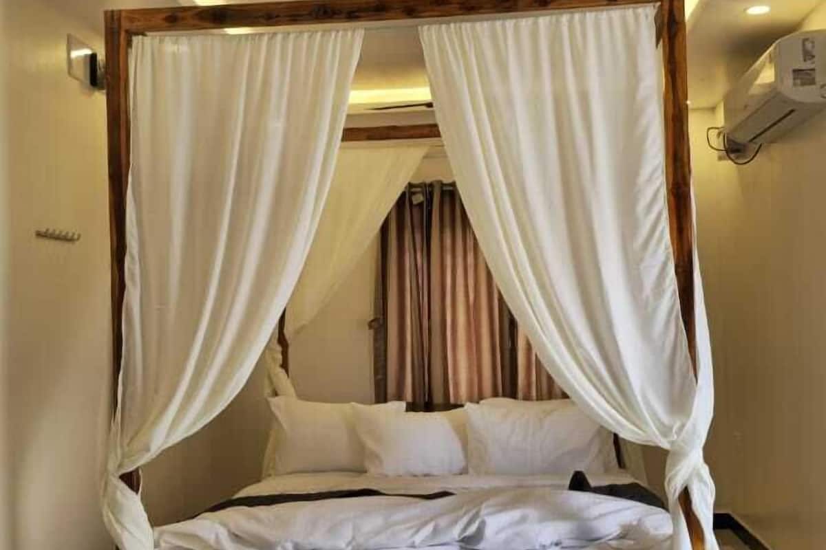A four-poster bed with white linens and drapes, a ceiling fan, and a tiled floor.