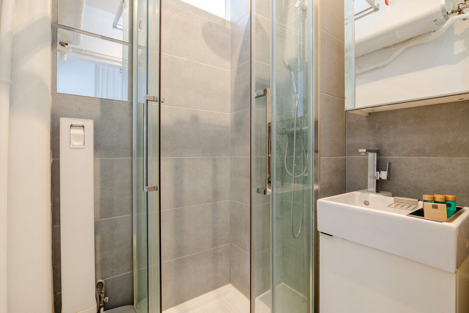 Un baño moderno con ducha de vidrio, un lavabo blanco con dispensador de jabón y un espejo sobre el lavabo.