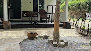 Una casa amb un porxo cobert, taula de menjador, cadires, una planta en test i un arbre.