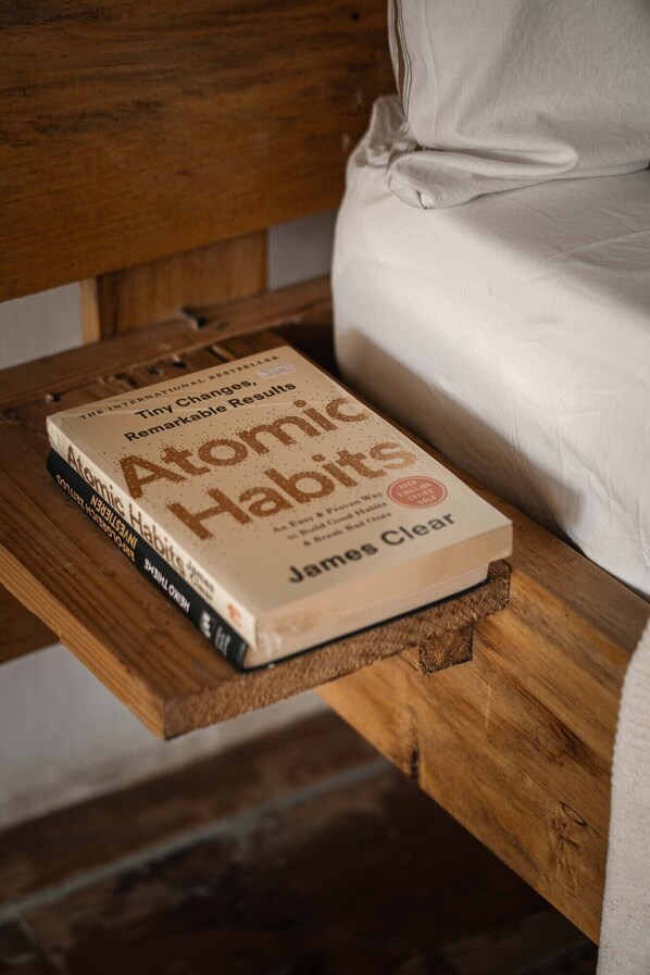Un libro titulado 'Atomic Habits' de James Clear sobre una estantería de madera en una habitación.