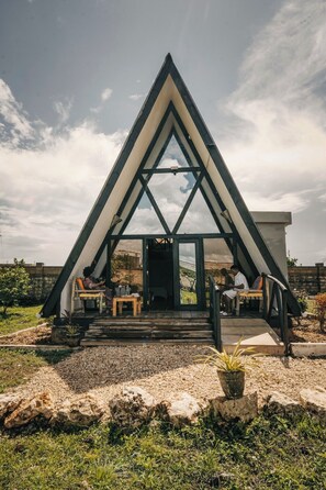 Un edificio triangular con una entrada central, mesas al aire libre y un camino de grava.