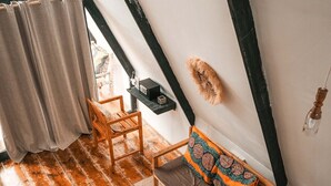 Ett loftliknande rum med synliga träbjälkar, en soffa med mönstrade kuddar, ett litet bord med ett bricka på och en hängande lampa.