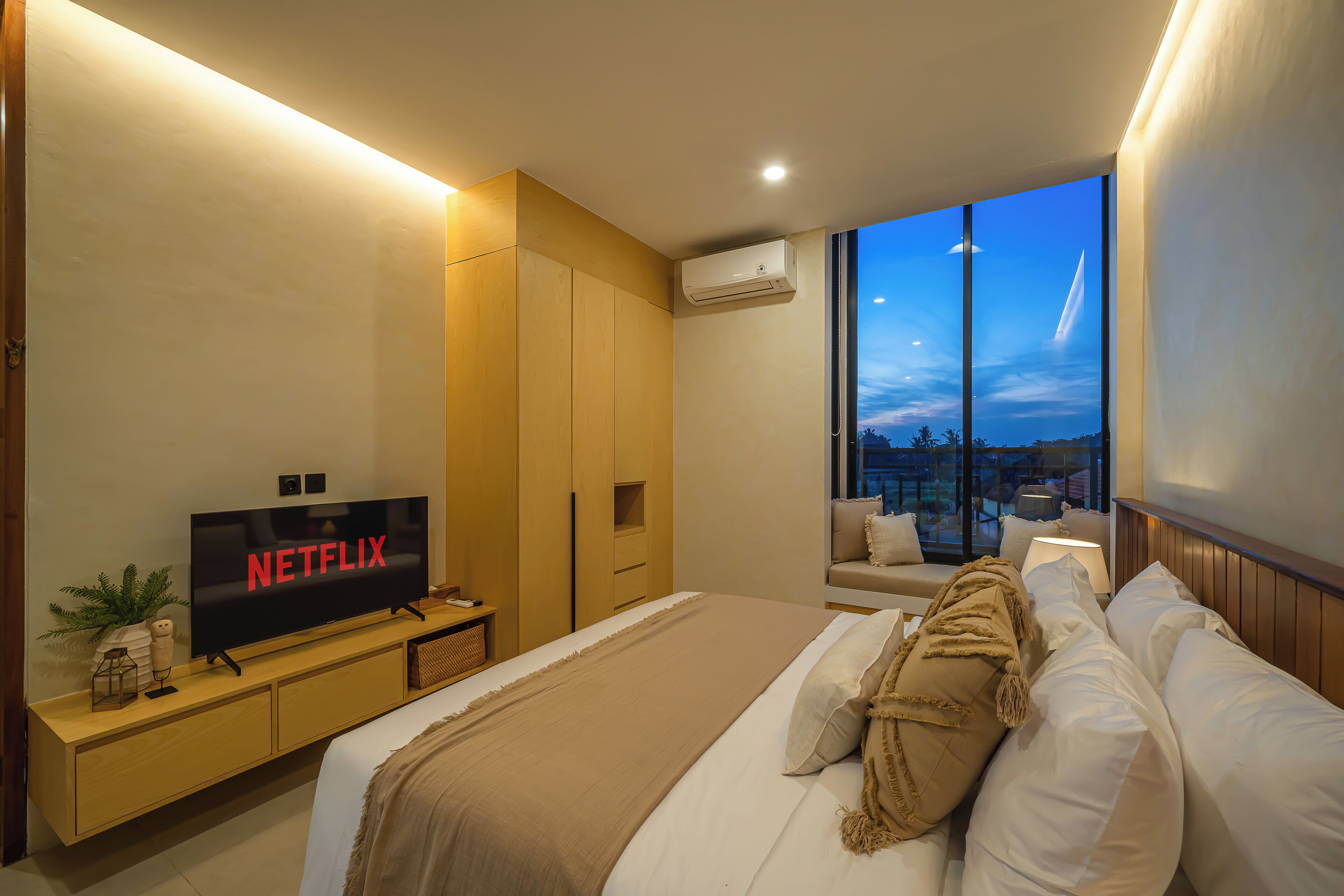A modern hotel room with a large bed, a TV displaying 'NETFLIX', a balcony with a view, and a wooden wardrobe.