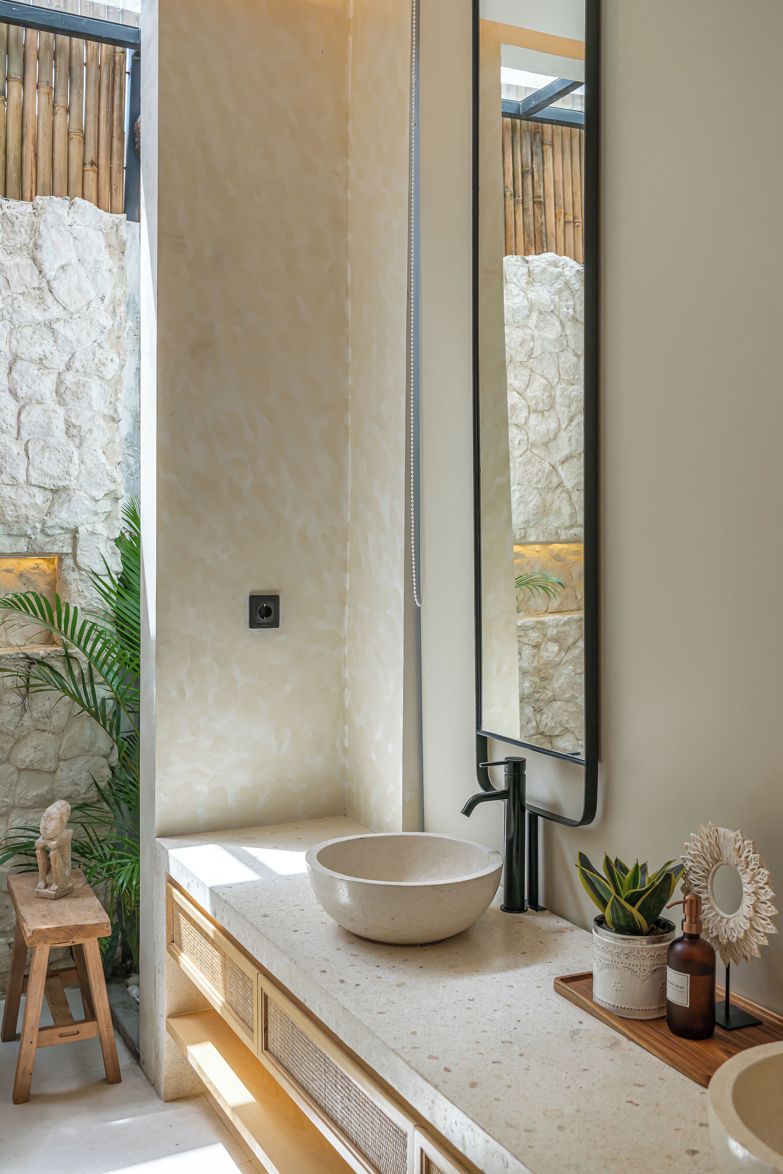 A bathroom with a large mirror, a stone wall, a wooden stool, and a bowl sink.