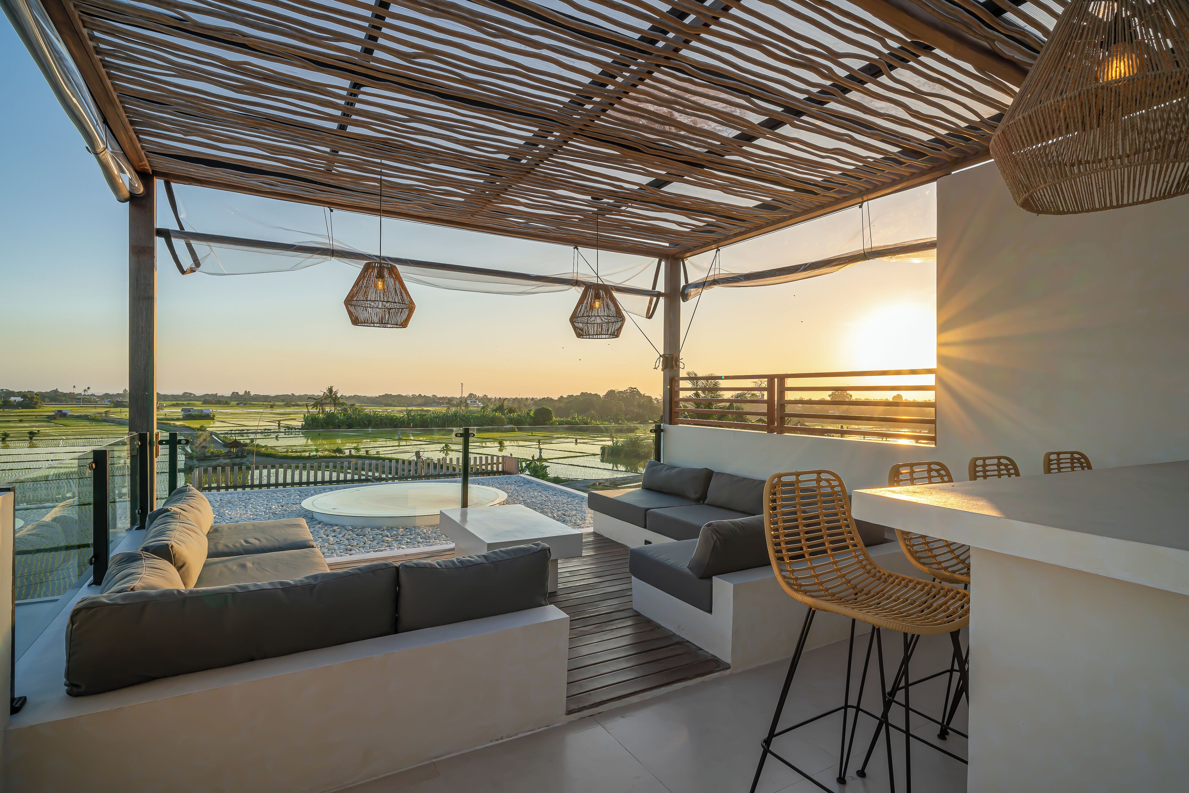 A covered outdoor seating area with a view of a golf course, a white table, and wicker chairs.