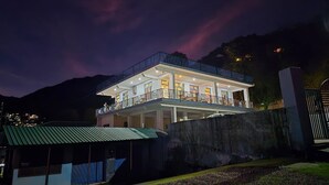 Un edificio a due piani con un balcone e numerose finestre, immerso in un'area verde e con una montagna sullo sfondo.