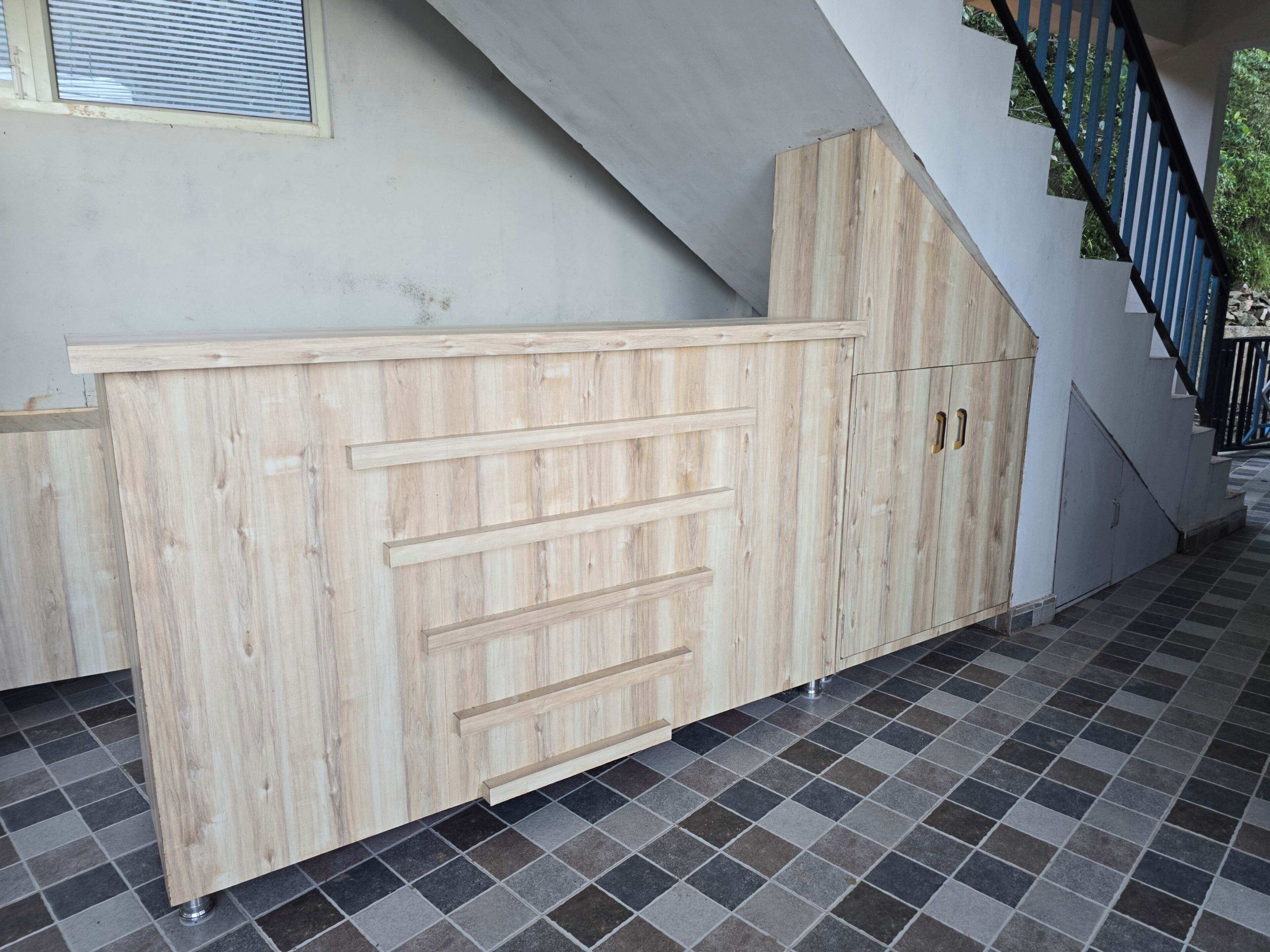 A wooden cabinet with drawers, a tiled floor, and a staircase with black railings.