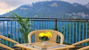 Un conjunto de silla y mesa de mimbre en un balcón con vistas a montañas y una barandilla azul.