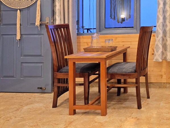A wooden dining table with two chairs, a blue door, and a window with curtains. - Aangan Royal Stay - Your Mountain Home in Dharamshala (Dharamshala)