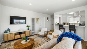 A modern living room with a TV, sofa, coffee table, and a kitchen area with bar stools.
