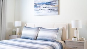 A bedroom with a bed, two bedside tables, a nightstand, a lamp, and a painting on the wall.
