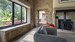 A rustic interior with exposed stone walls, a fireplace, and a large window overlooking a garden.