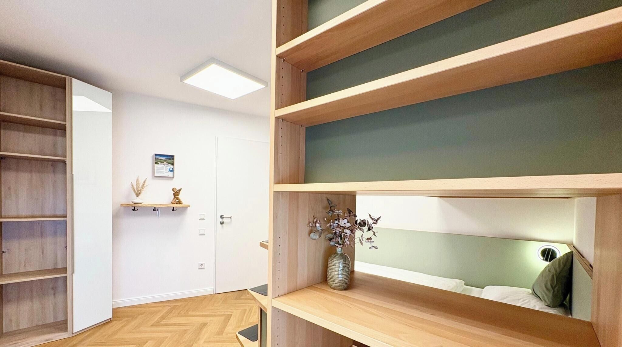 Une pièce moderne avec des étagères en bois intégrées, une porte et une petite étagère ornée d’objets décoratifs.